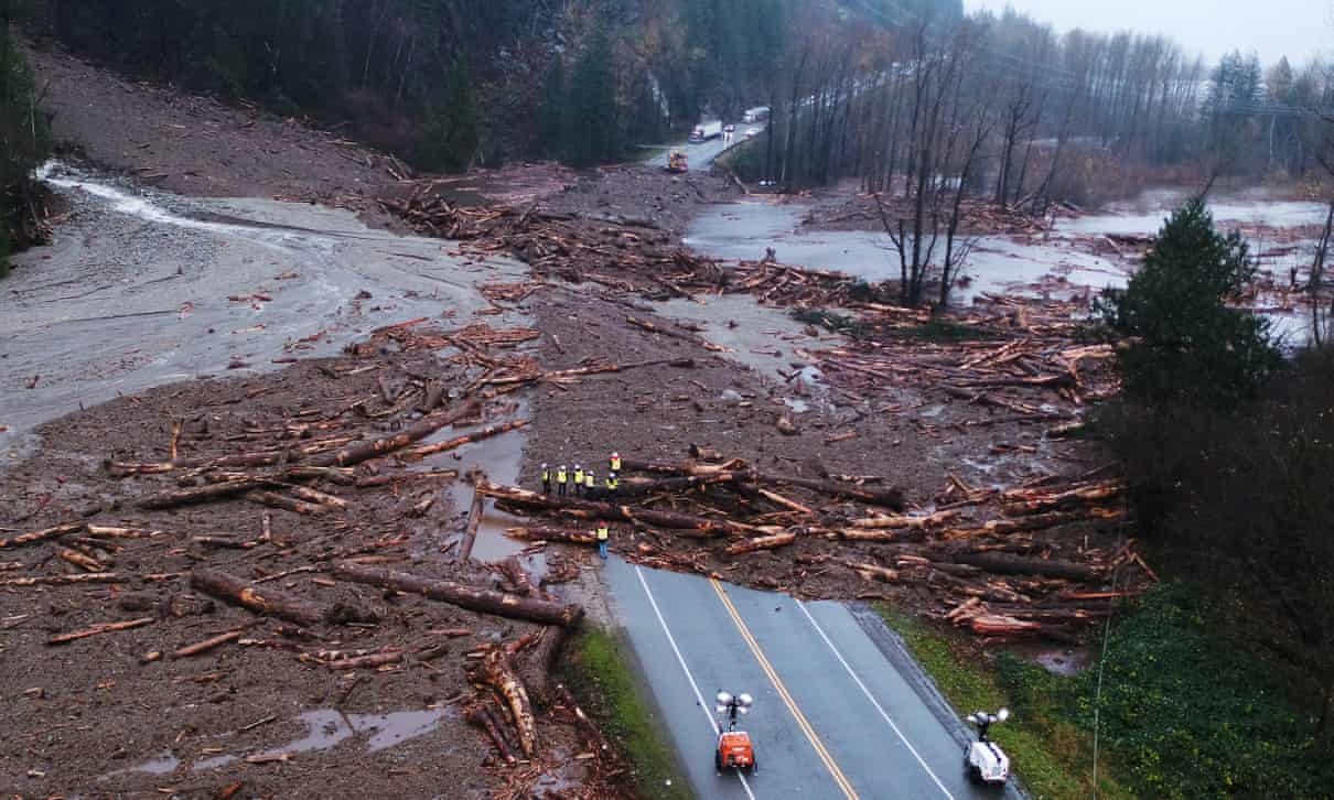 The debris flows from left to right from the top of a hill/ mountain, across a road and into a river. The debris includes visible destroyed pieces of trees, mud and water. The road is impassable. The area is contained to a specific location.